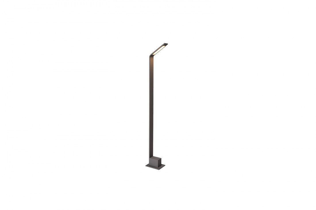 Na obrazie widoczna jest smukła, nowoczesna lampa ogrodowa w formie słupka, wykonana z ciemnego materiału. Lampa ma prosty design z lekko nachyloną górną częścią, w której znajduje się źródło światła.