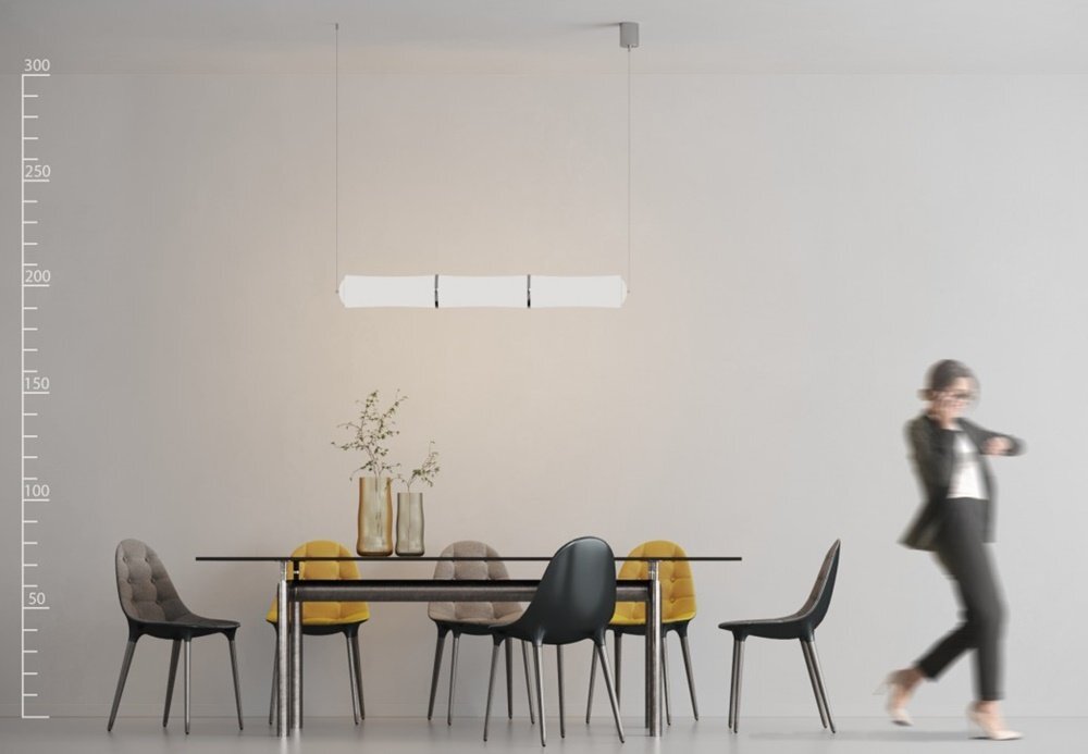 Na obrazie znajduje się nowoczesna lampa wisząca nad stołem z sześcioma krzesłami w różnych kolorach. W tle widać osobę w ruchu oraz dekoracyjne wazony na stole.
