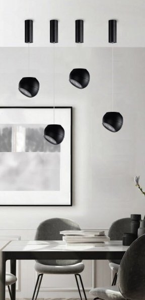 Na obrazie widać nowoczesne, czarne lampy wiszące nad stołem w eleganckim wnętrzu. W tle znajduje się duży obraz oraz krzesła przy stole.