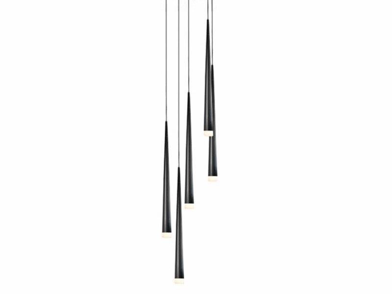 Na obrazie widoczna jest lampa wisząca z pięcioma smukłymi, czarnymi kloszami zwisającymi na cienkich przewodach. Każdy klosz zakończony jest jasnym źródłem światła.