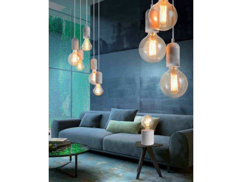 Wnętrze z nowoczesnym wystrojem, w którym znajduje się szara sofa z poduszkami oraz stolik z lampą o dużych żarówkach. W tle widoczne są wiszące lampy z przezroczystymi kloszami, emitujące ciepłe światło.