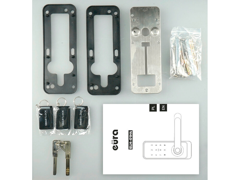 Na obrazie widoczne są elementy montażowe klamki, w tym metalowe i plastikowe części, trzy breloki z napisem \'SMART LOCK\', klucze oraz instrukcja z logo \'eura\' i oznaczeniem \'ELH-01H4\'.