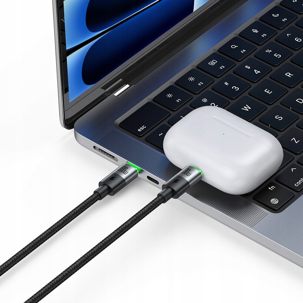 Na obrazie widać laptop z podłączonymi dwoma kablami USB-C, które mają zielone podświetlenie. Obok laptopa leży białe etui na słuchawki bezprzewodowe.