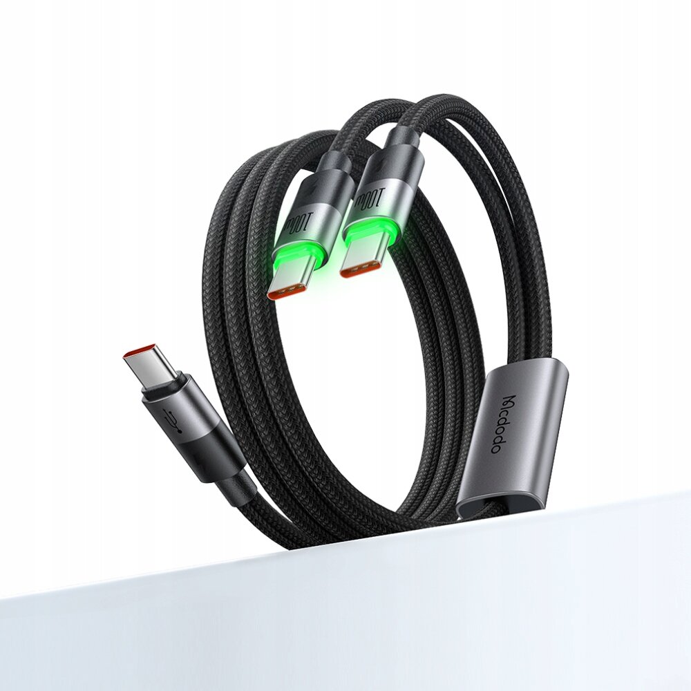 Na obrazie widoczny jest czarny, pleciony kabel USB-C z dwoma końcówkami, które mają zielone podświetlenie. Na jednej z końcówek widnieje napis \'Mcdodo\'.