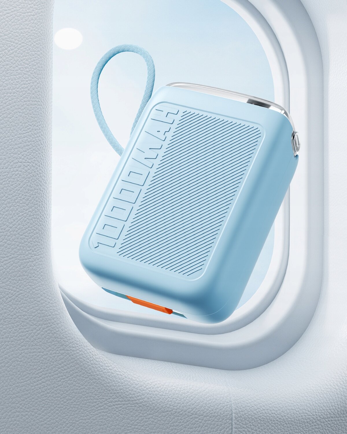 Niebieski powerbank z napisem \'10000MAH\' widoczny przez okno samolotu. Powerbank ma zaokrąglone krawędzie i pomarańczowy element na dole.
