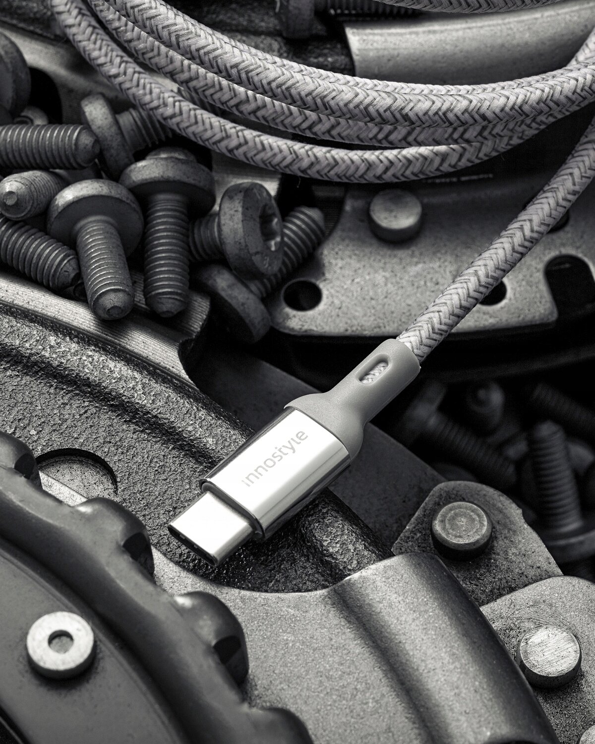 Srebrny kabel USB-C z napisem \'innostyle\' leży na tle metalowych elementów i śrub. Kabel ma plecioną osłonę i metalowe złącze.