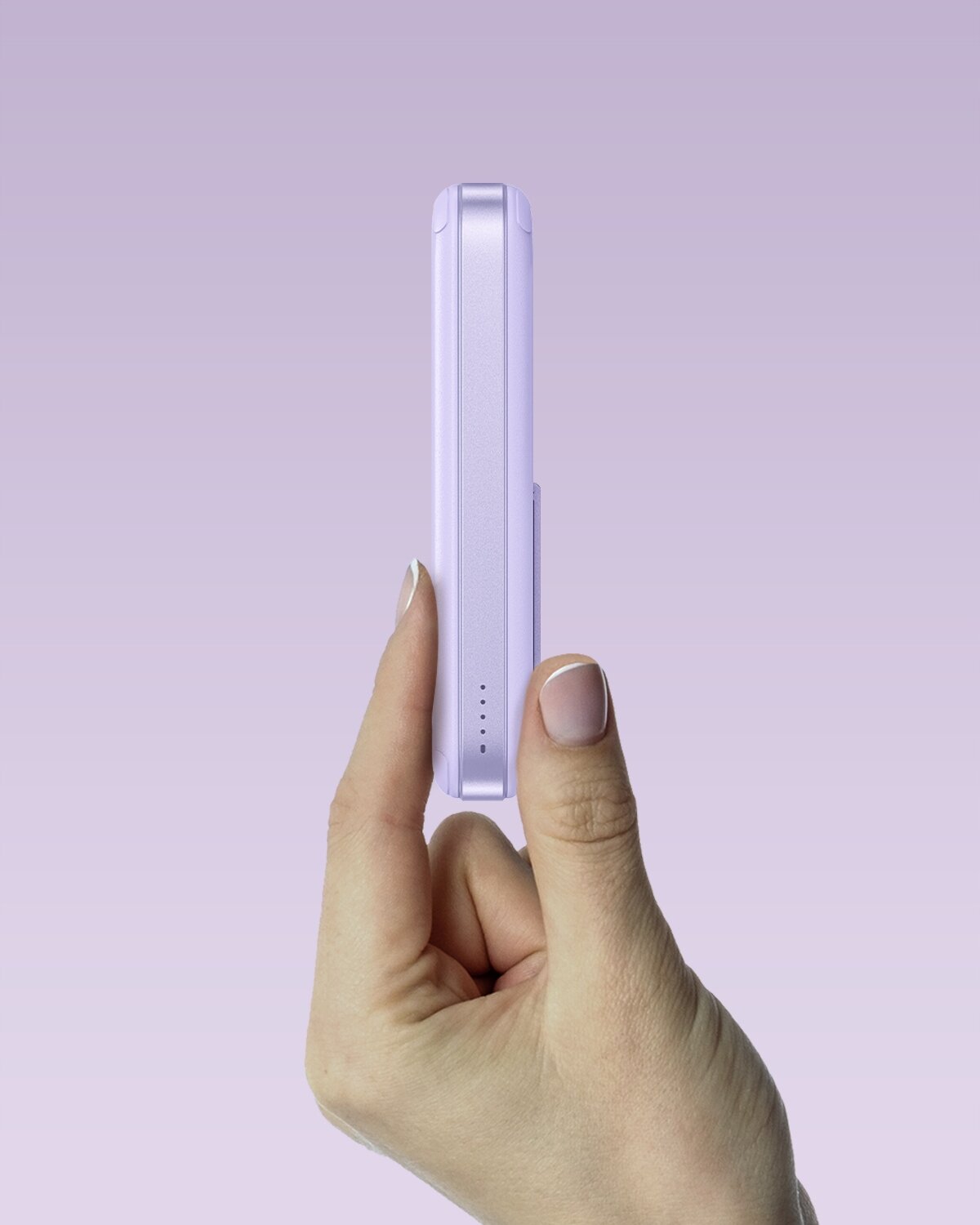 Osoba trzyma fioletowy powerbank w dłoni na tle w odcieniach fioletu. Na urządzeniu widoczne są cztery małe diody sygnalizacyjne.