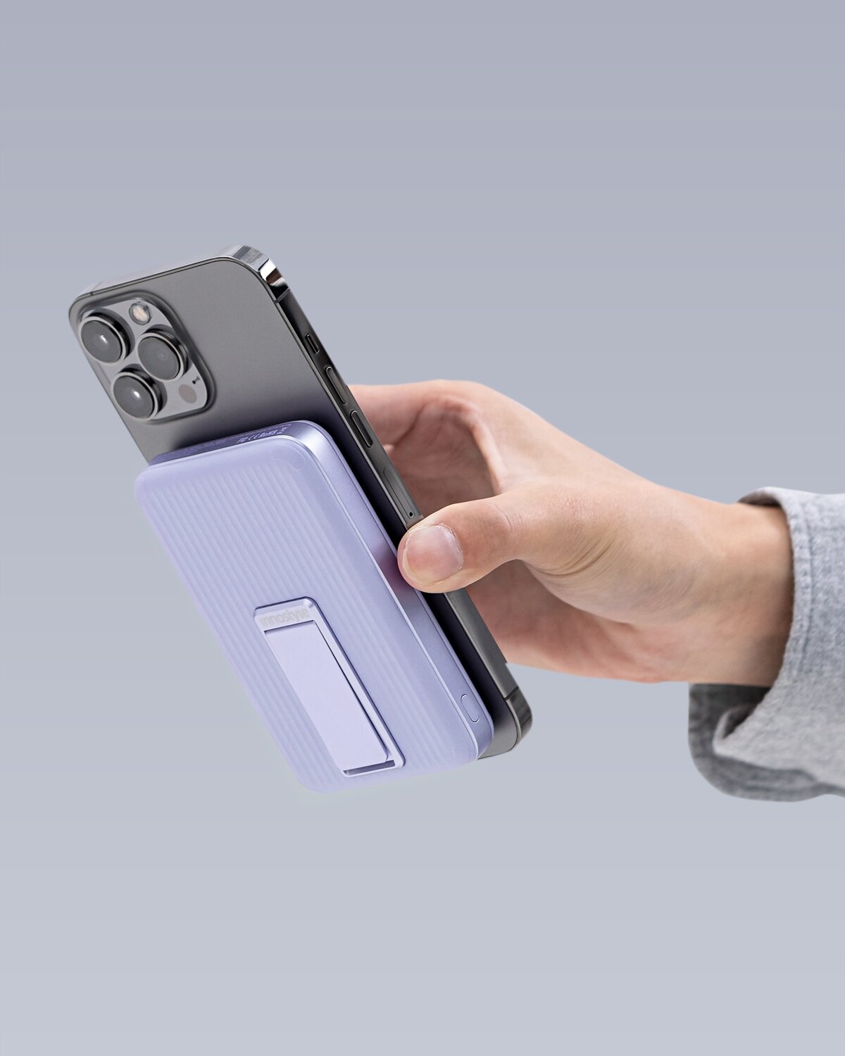 Osoba trzyma smartfon z przymocowanym fioletowym powerbankiem indukcyjnym, który ma wbudowany stojak.