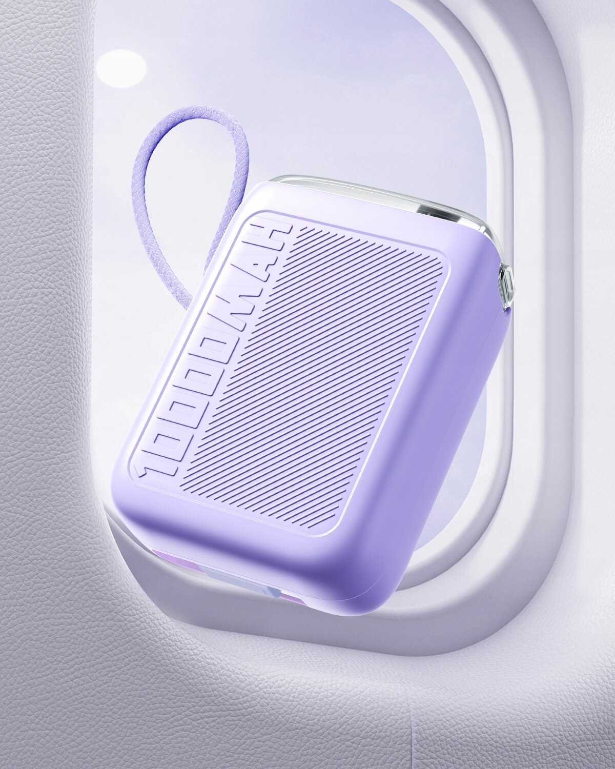 Fioletowy powerbank z napisem \'10000MAH\' wisi przy oknie samolotu. Ma teksturowaną powierzchnię i zaokrąglone krawędzie.