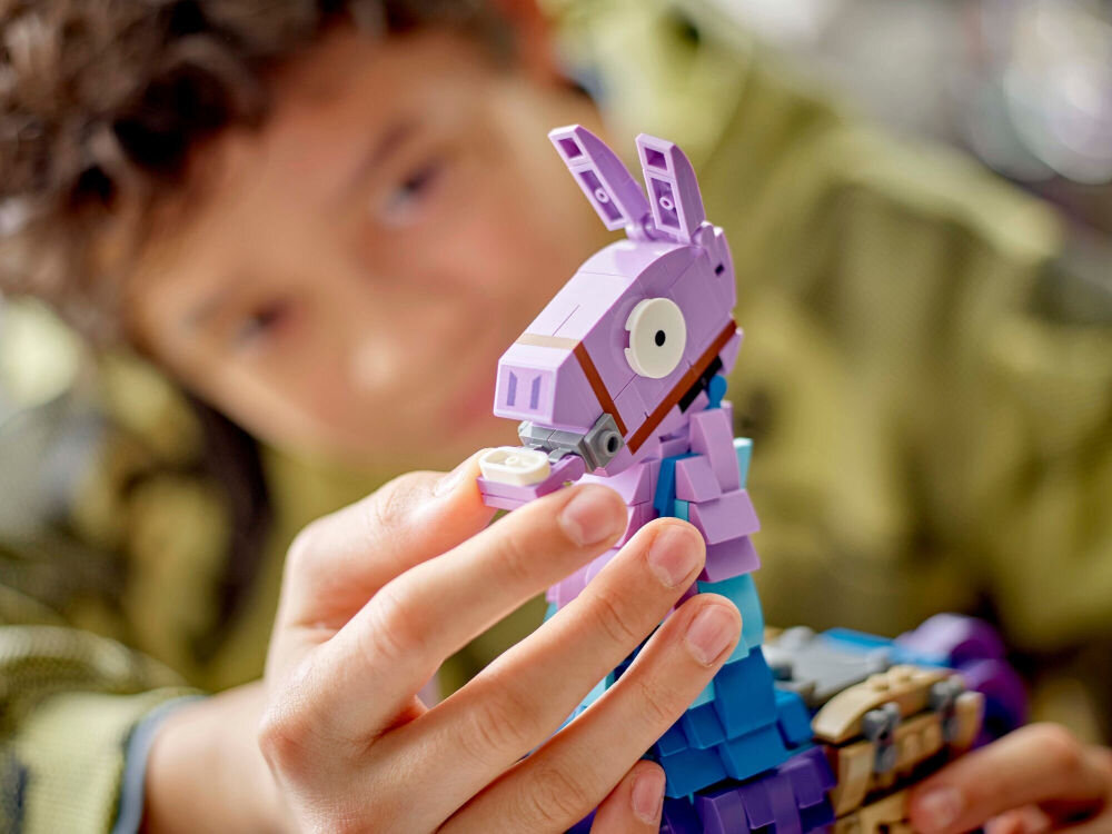 Osoba trzyma model z klocków LEGO przedstawiający fioletową lamę z gry Fortnite. Llama jest zbudowana z klocków w kolorach fioletowym, niebieskim i brązowym.