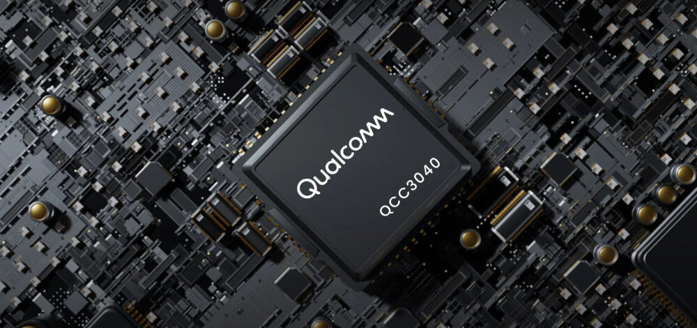 Obraz przedstawia zbliżenie na układ scalony z widocznym napisem \'Qualcomm QCC3040\'. W tle widać skomplikowaną strukturę elektroniczną z elementami w kolorze czarnym i złotym.
