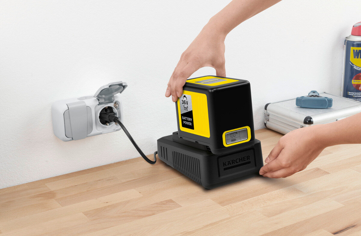 Osoba umieszcza akumulator KARCHER na ładowarce podłączonej do gniazdka elektrycznego. Na akumulatorze widoczny jest napis \'36V BATTERY POWER\'.