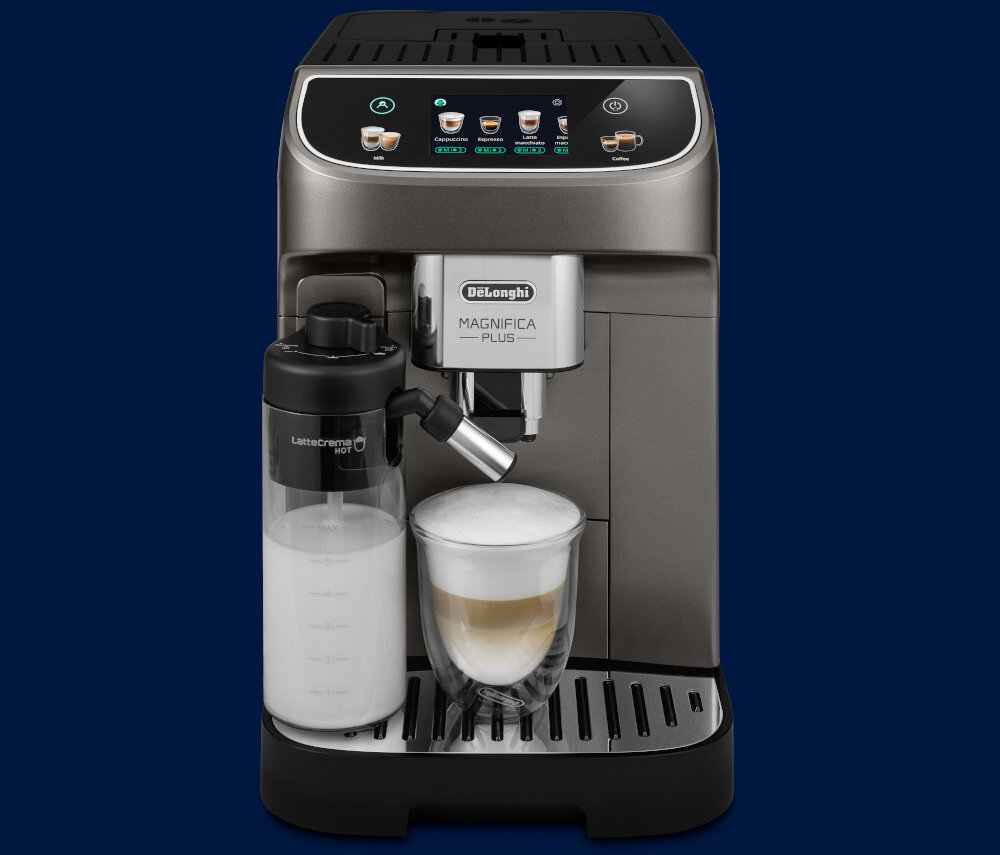Ekspres do kawy z wyświetlaczem i przyciskami dotykowymi na górze, obok pojemnik na mleko z napisem \'LatteCrema HOT\'. Na tacy ociekowej stoi szklanka z kawą z pianką, a na ekspresie widoczne jest logo \'DeLonghi Magnifica Plus\'.