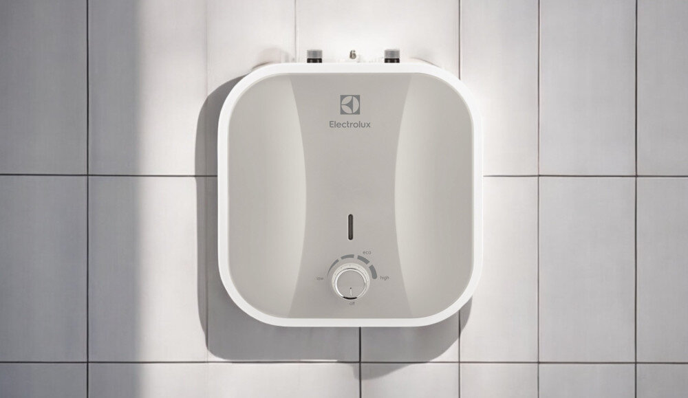 Na obrazie widoczny jest biały bojler elektryczny z logo Electrolux, zamontowany na ścianie z płytek. Na bojlerze znajduje się pokrętło z oznaczeniami temperatury: low, eco, high.