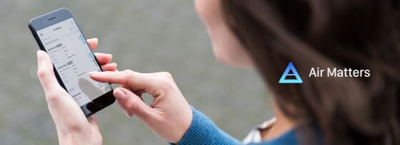 Osoba trzyma smartfon z aplikacją na ekranie. Obok widoczne jest logo w kształcie trójkąta i napis \'Air Matters\'.