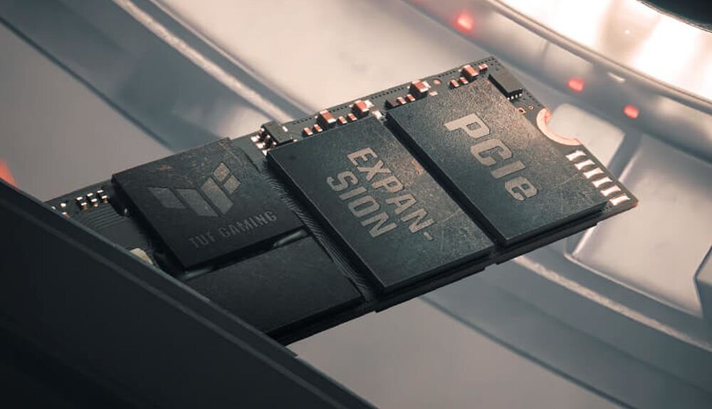 Obraz przedstawia moduł pamięci z widocznymi napisami: \'TUF GAMING\', \'EXPANSION\' i \'PCIe\'. Moduł jest umieszczony w futurystycznym otoczeniu z metalicznymi elementami.