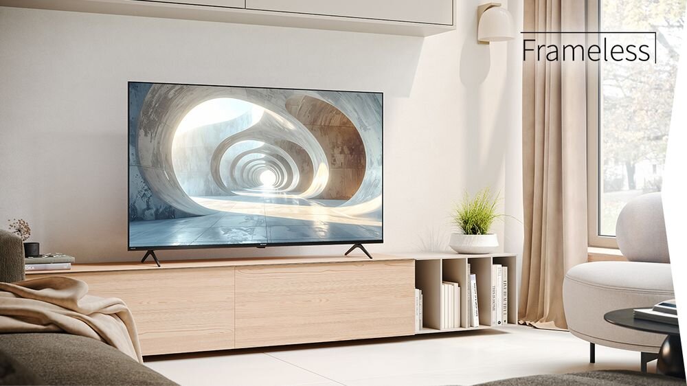 Telewizor z cienkimi ramkami stoi na drewnianej szafce w nowoczesnym salonie. Na ekranie wyświetlany jest obraz tunelu, a w rogu widoczny jest napis \'Frameless\'.