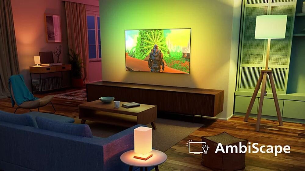 W salonie znajduje się telewizor wyświetlający kolorowy obraz, z efektem Ambilight na ścianie. W pomieszczeniu są także meble, lampa stojąca i stolik z lampką.