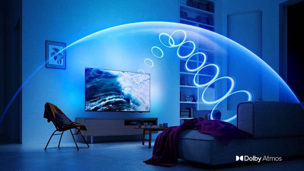 Pokój z telewizorem wyświetlającym obraz fal morskich, otoczony niebieskim światłem. W prawym dolnym rogu widoczne jest logo \'Dolby Atmos\'.
