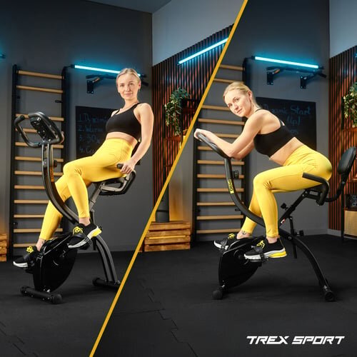 Dwie kobiety ćwiczą na czarnym rowerku stacjonarnym w pomieszczeniu z drewnianymi elementami i neonowym oświetleniem. Na dole widoczne jest logo \'TREX SPORT\'.