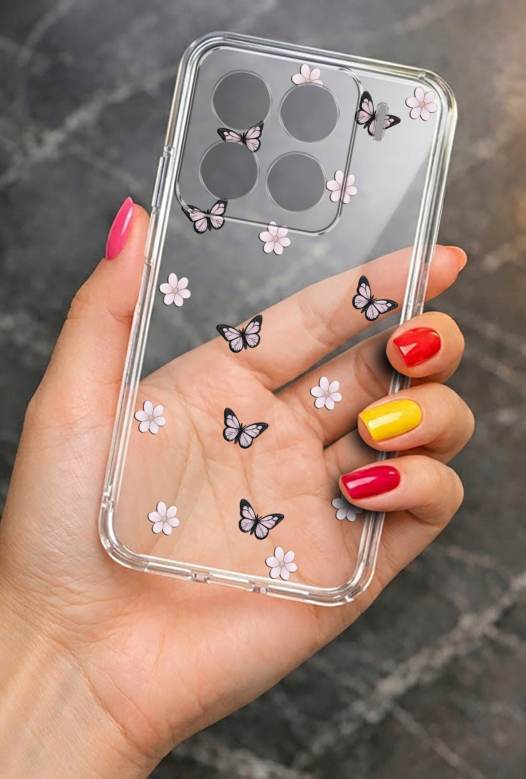 Przezroczyste etui na telefon z motywem motyli i kwiatów trzymane w dłoni z kolorowymi paznokciami. Etui ma wycięcia na cztery obiektywy aparatu.