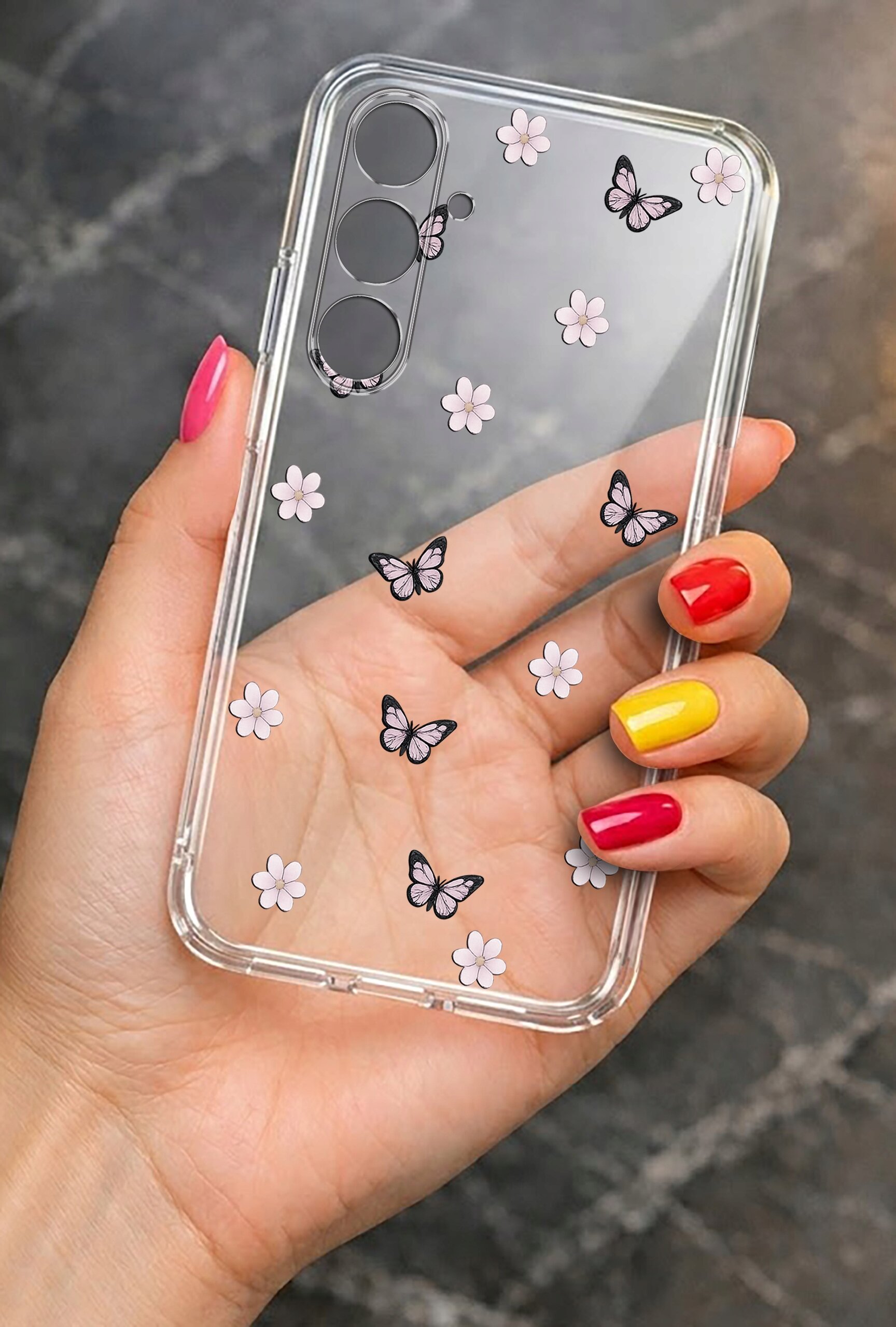 Przezroczyste etui na telefon z motywem różowych kwiatów i motyli. Osoba trzymająca etui ma pomalowane paznokcie w kolorach różowym, czerwonym i żółtym.
