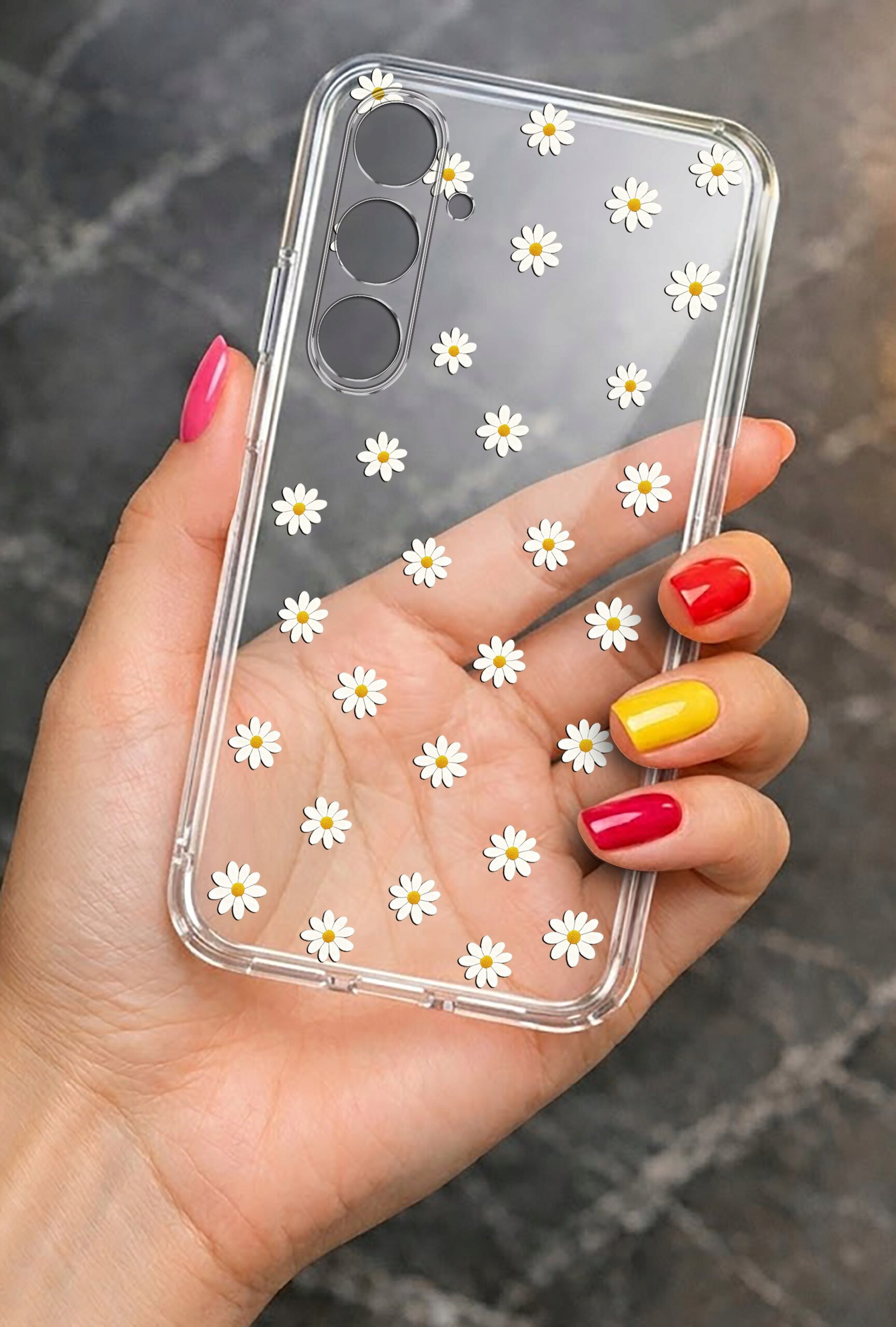Przezroczyste etui na telefon z wzorem białych stokrotek trzymane w dłoni z kolorowymi paznokciami. Etui ma wycięcia na trzy obiektywy aparatu.