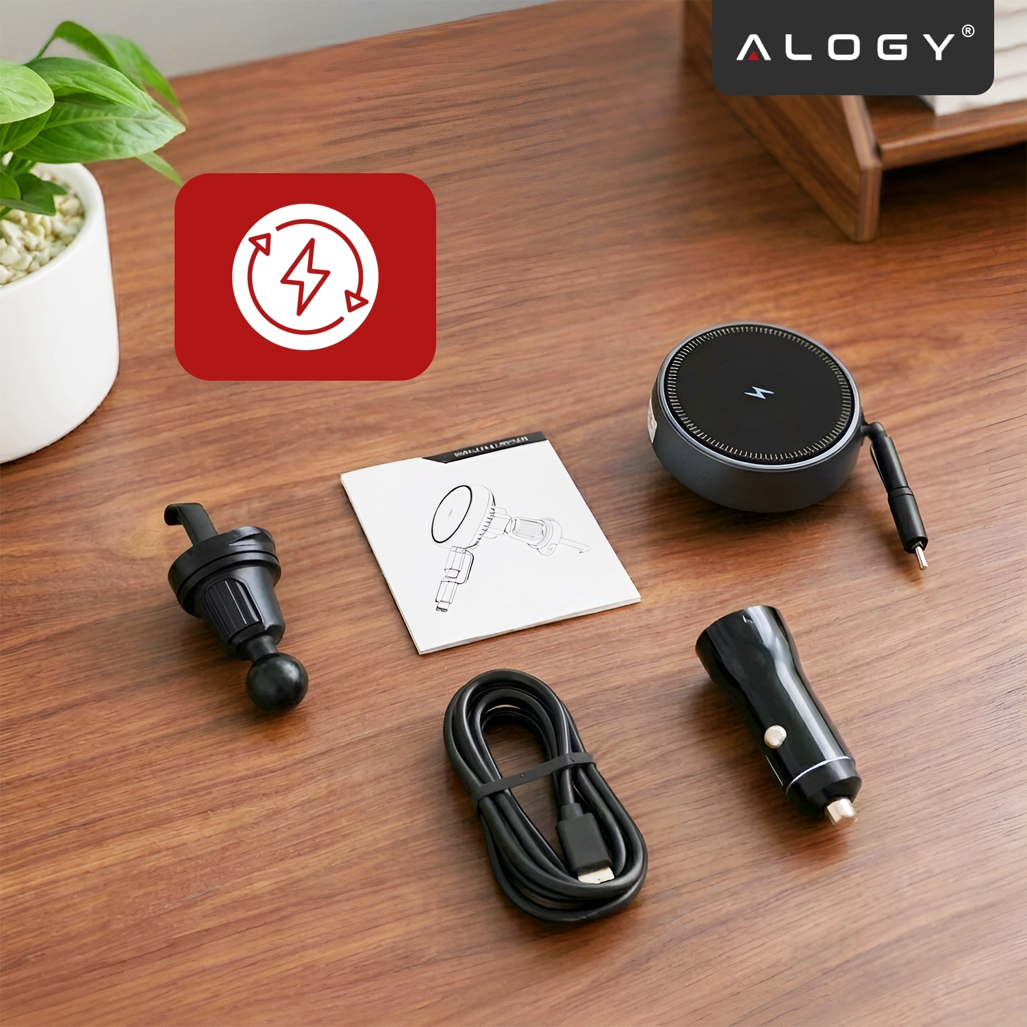 Na drewnianym blacie znajdują się elementy uchwytu samochodowego do kratki, ładowarka indukcyjna, kabel USB-C oraz instrukcja obsługi. W prawym górnym rogu widoczne jest logo \'ALOGY\'.