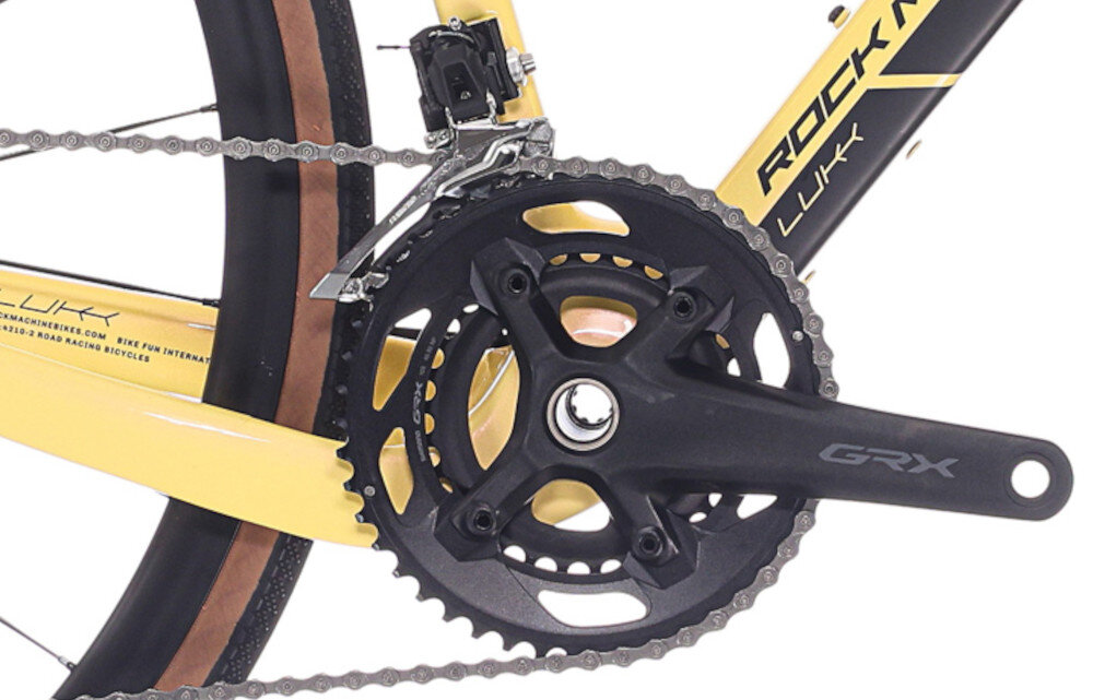 Rower gravel ROCK MACHINE Lukk Cr 65 U20 28 cali Żółty zbliżenie na korbę białe tło wkład suportu SHIMANO typu BSA korba SHIMANO typu FC-U6030-2 o zakresie zębów 46-32T kaseta SHIMANO typu CS-LG400, 10-speed o zakresie 11–39T odpowiednie przełożenie szeroki zakres kasety odpowiednio dobrane komponenty