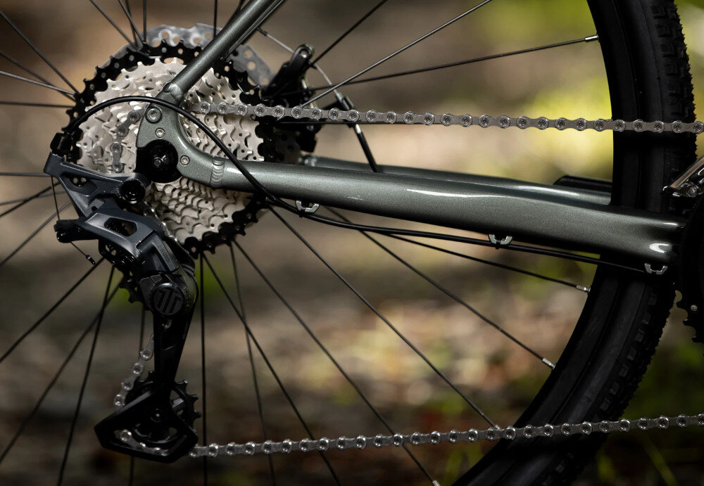 Rower gravel ROCK MACHINE Lukk 40 U19 28 cali Zielony rozmazane tło zbliżenie na tylną przerzutkę przerzutki MicroSHIFT FD-G7020 E-Type z przodu i RD-G7025L z tyłu szeroki zakres przełożeń (20  biegów) komfortowa kadencja łatwiej zachować rytm jazdy