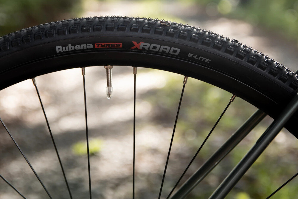 Rower gravel ROCK MACHINE Lukk 40 U20 28 cali Zielony rozmazane tło zbliżenie na oponę rozmiar koła 28 cali łatwiej jest pokonać różne przeszkody opony marki RUBENA obręcze marki Stars J20 piasty SHIMANO typu HB-QC300 regularne sprawdzanie ciśnienia powietrza wartość na bocznej części opony