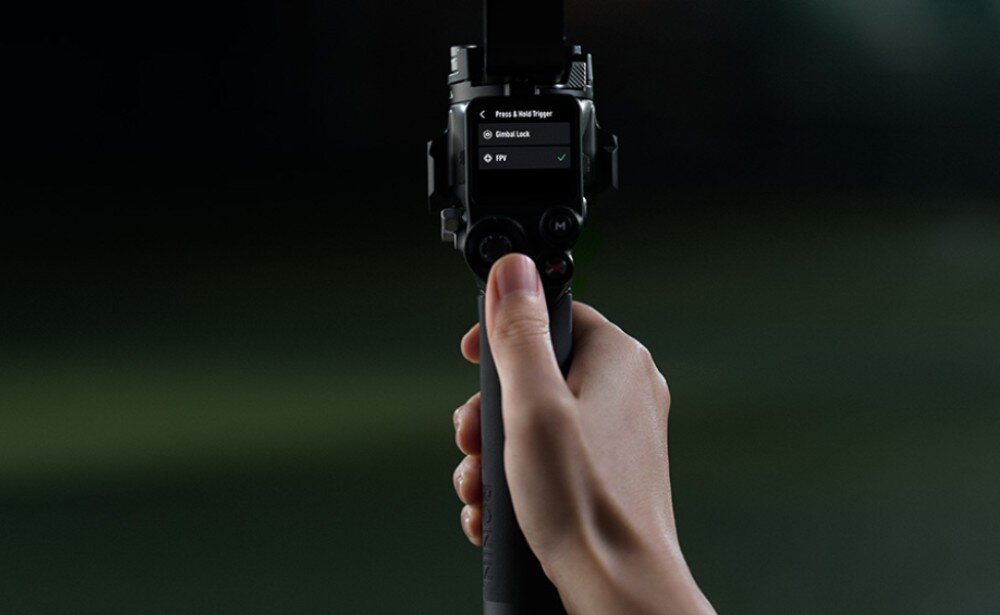 Osoba trzyma urządzenie z wyświetlaczem pokazującym opcje: \'Press & Hold Trigger\', \'Gimbal Lock\', \'FPV\'.