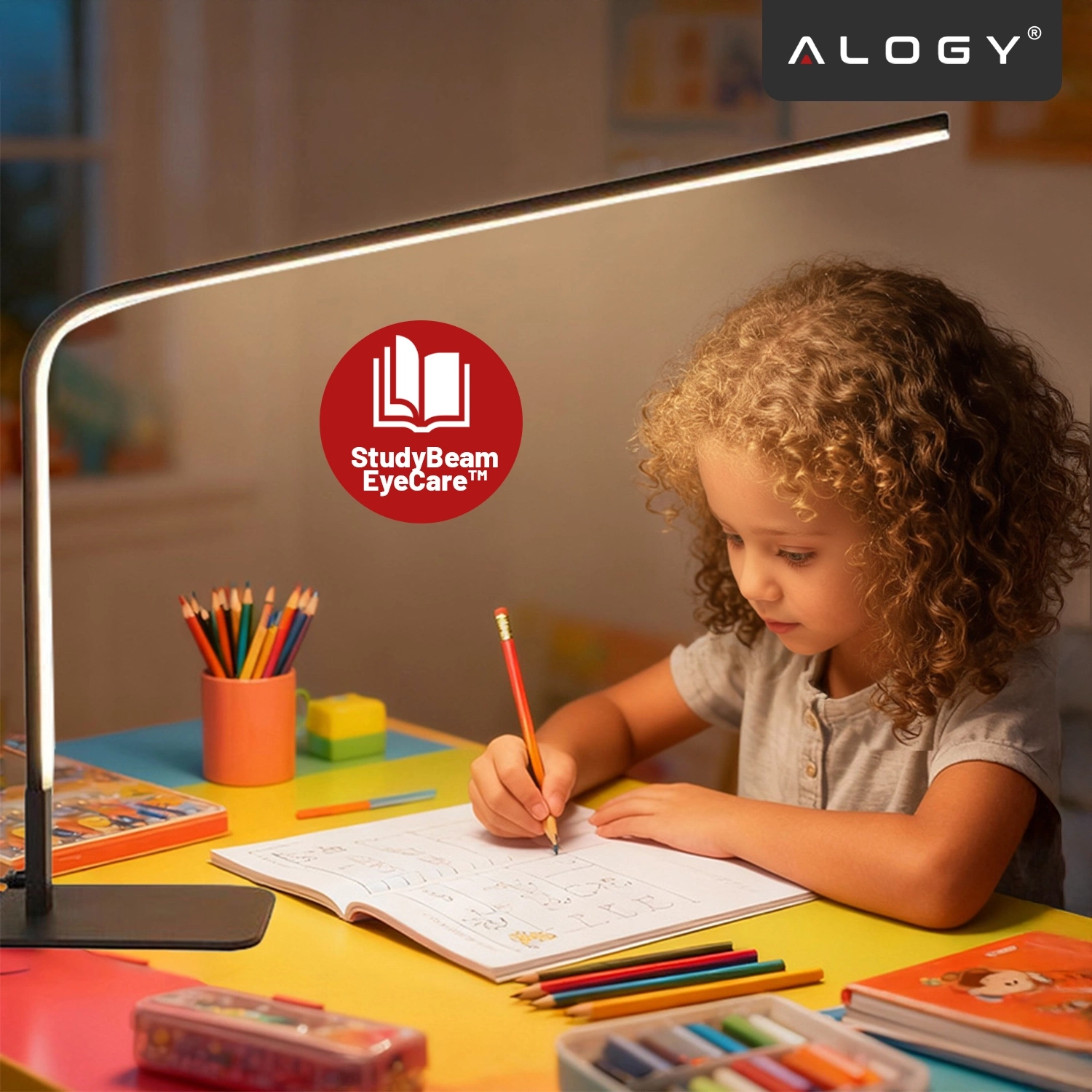 Na biurku znajduje się czarna lampka biurkowa LED, oświetlająca dziecko rysujące w zeszycie. W tle widoczne są kolorowe kredki i przybory szkolne, a w rogu logo \'ALOGY\' oraz napis \'StudyBeam EyeCare™\'.