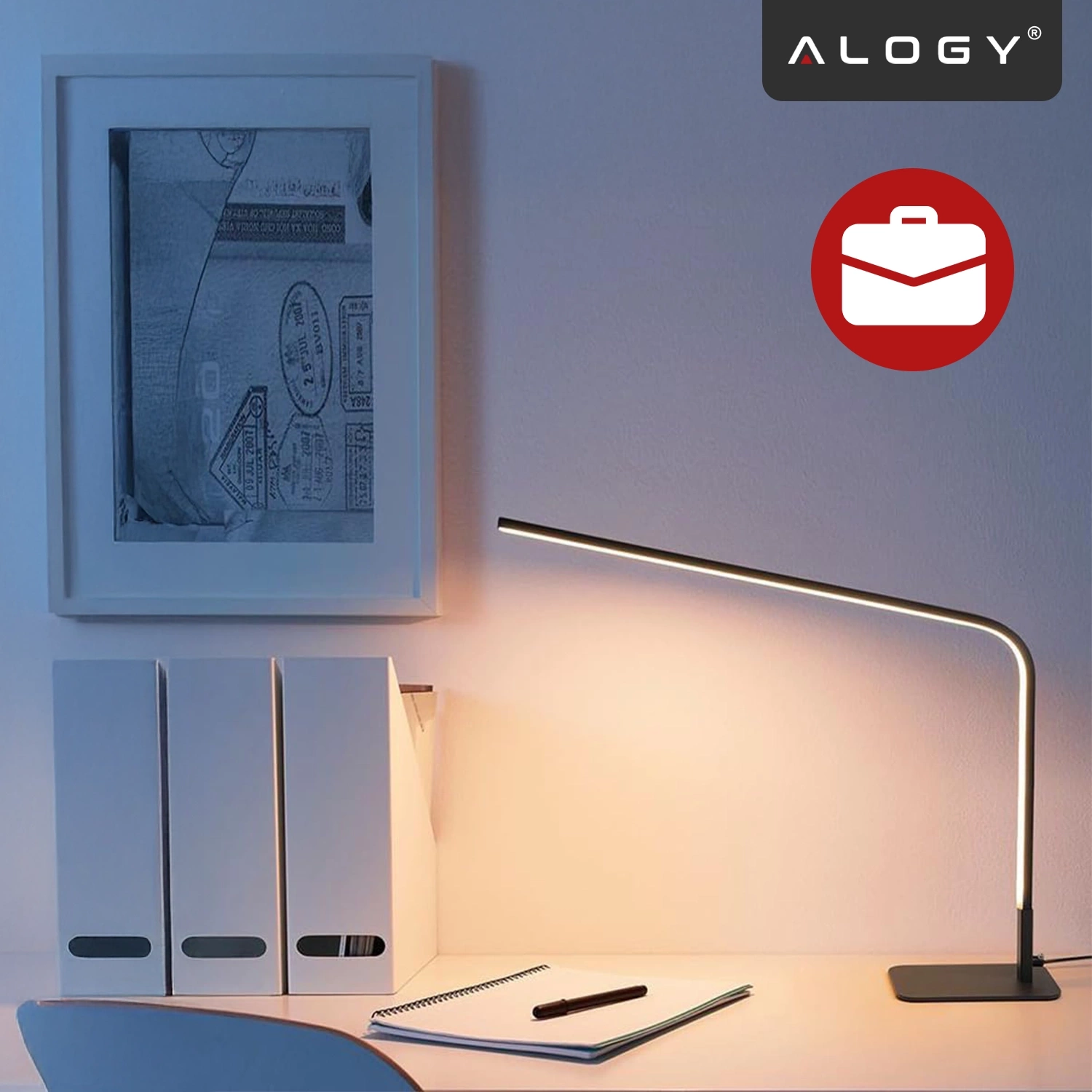 Na biurku znajduje się czarna lampka biurkowa LED o nowoczesnym designie, obok której leży zeszyt i długopis. Na ścianie wisi obraz, a w rogu widoczne jest logo \'ALOGY\'.