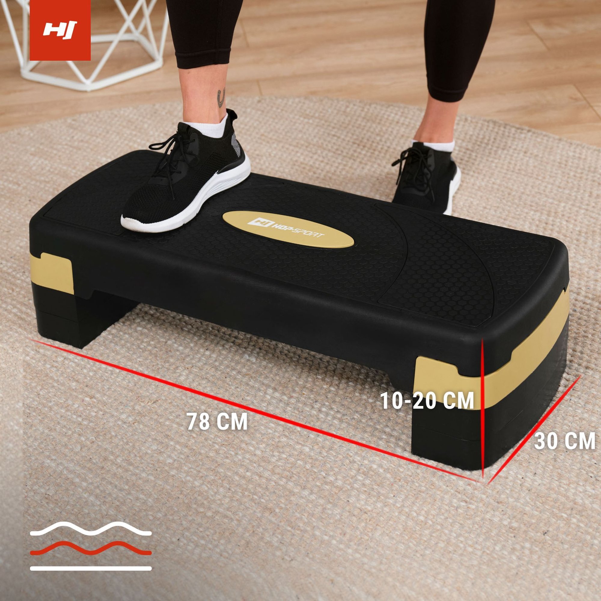 Czarno-złoty step do ćwiczeń z logo \'HOP SPORT\' na środku, z jedną stopą w czarnym bucie na powierzchni. Wymiary stepu to 78 cm długości, 30 cm szerokości i regulowana wysokość 10-20 cm.