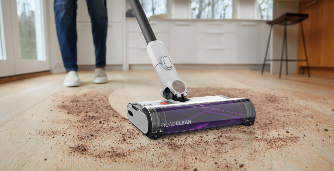 Odkurzacz z napisem \'QUADCLEAN\' zbiera rozsypane zanieczyszczenia z drewnianej podłogi w jasnej kuchni.