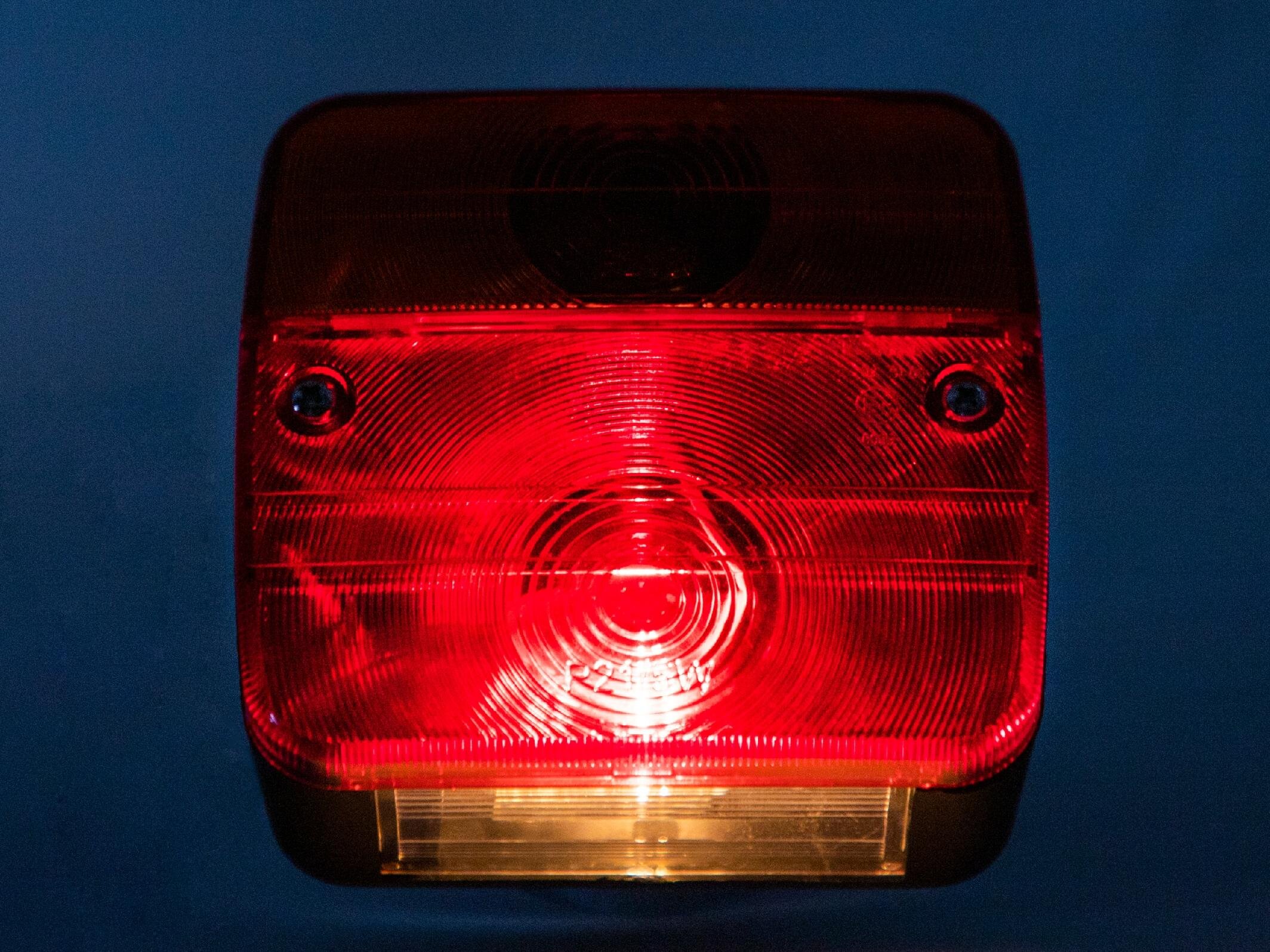 Czerwono-przezroczysta lampa zespolona z widocznymi okrągłymi wzorami i śrubami mocującymi. Na środku widoczny jest napis \'24V\'.