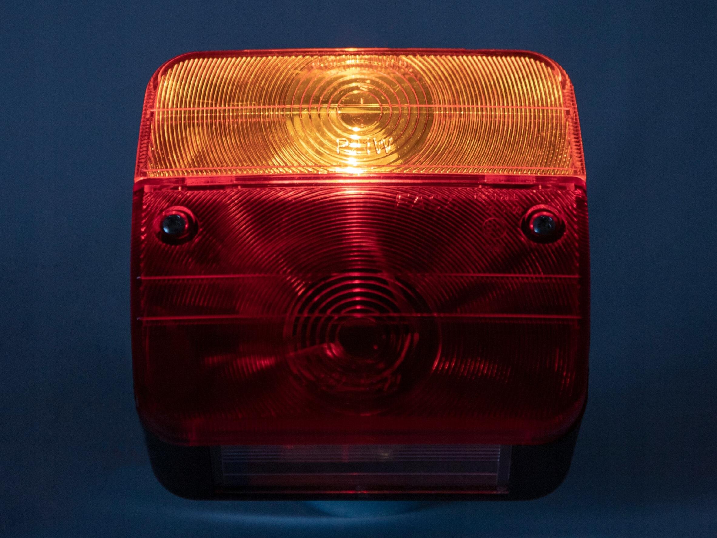Lampa zespolona z przezroczystym kloszem w kolorach pomarańczowym i czerwonym, z widocznymi okrągłymi wzorami. Na pomarańczowej części widoczny jest napis \'PMMA\'.