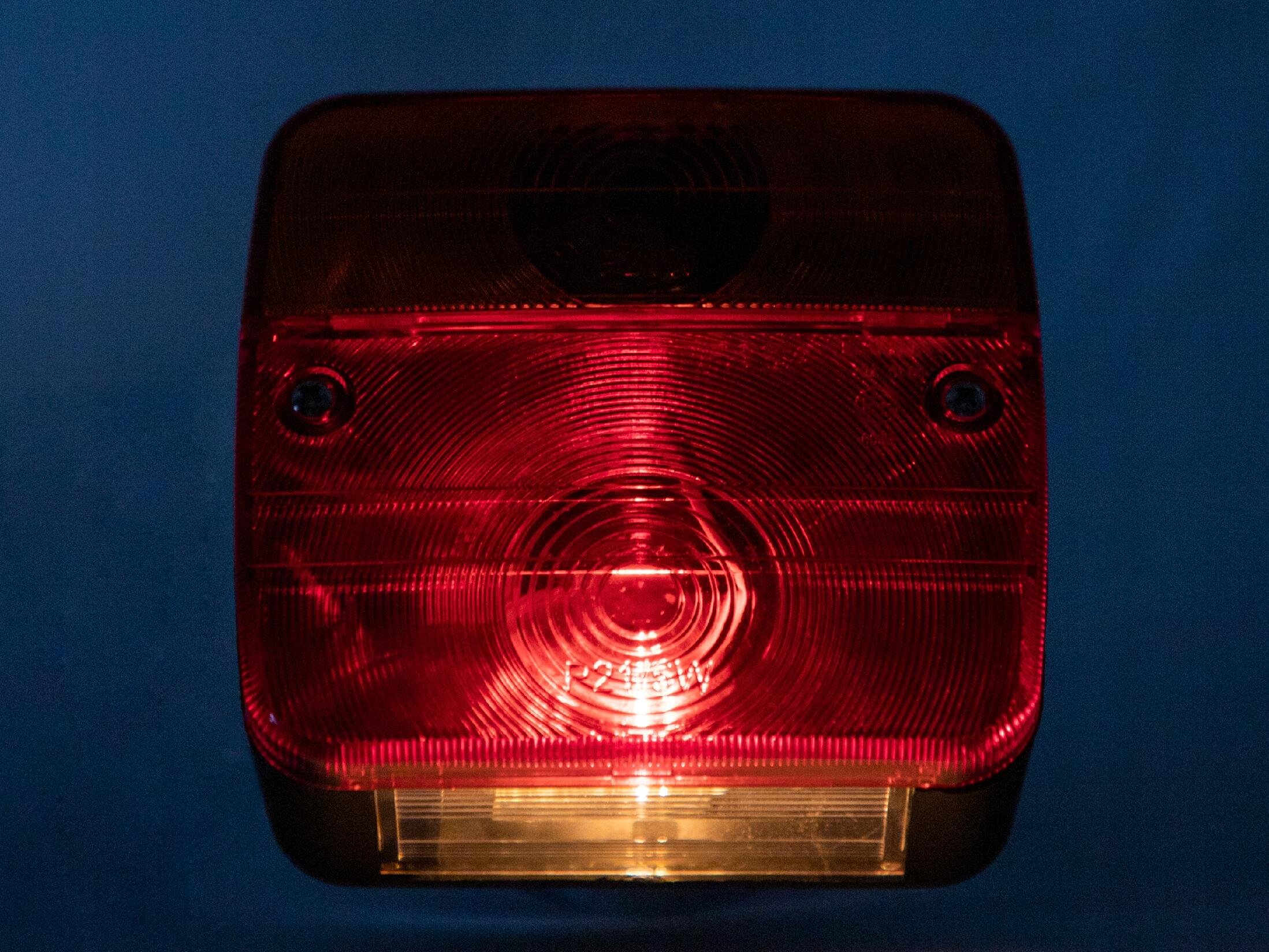 Czerwono-przezroczysta lampa zespolona z widocznymi okrągłymi wzorami i żarówką wewnątrz. Na powierzchni widoczny jest napis \'12V 5W\'.