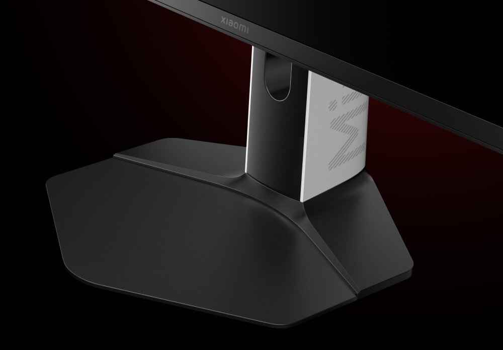 Monitor XIAOMI G Pro 27Qi Zbliżenie na czarną podstawę monitora o sześciokątnym kształcie. Podstawa łączy się z jasnoszarą nogą, na której widać fragment szarego napisu, regulacja, ergonomia