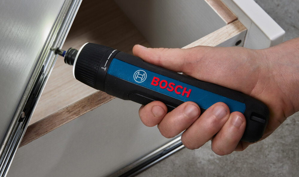 Osoba trzyma wkrętak akumulatorowy z widocznym logo BOSCH, używając go do montażu elementu meblowego.