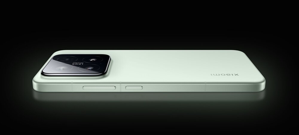 Na obrazie widoczny jest smartfon w kolorze jasnym, leżący na płaskiej powierzchni. Na obudowie znajduje się napis \'xiaomi\', a aparat fotograficzny jest umieszczony w lewym górnym rogu.