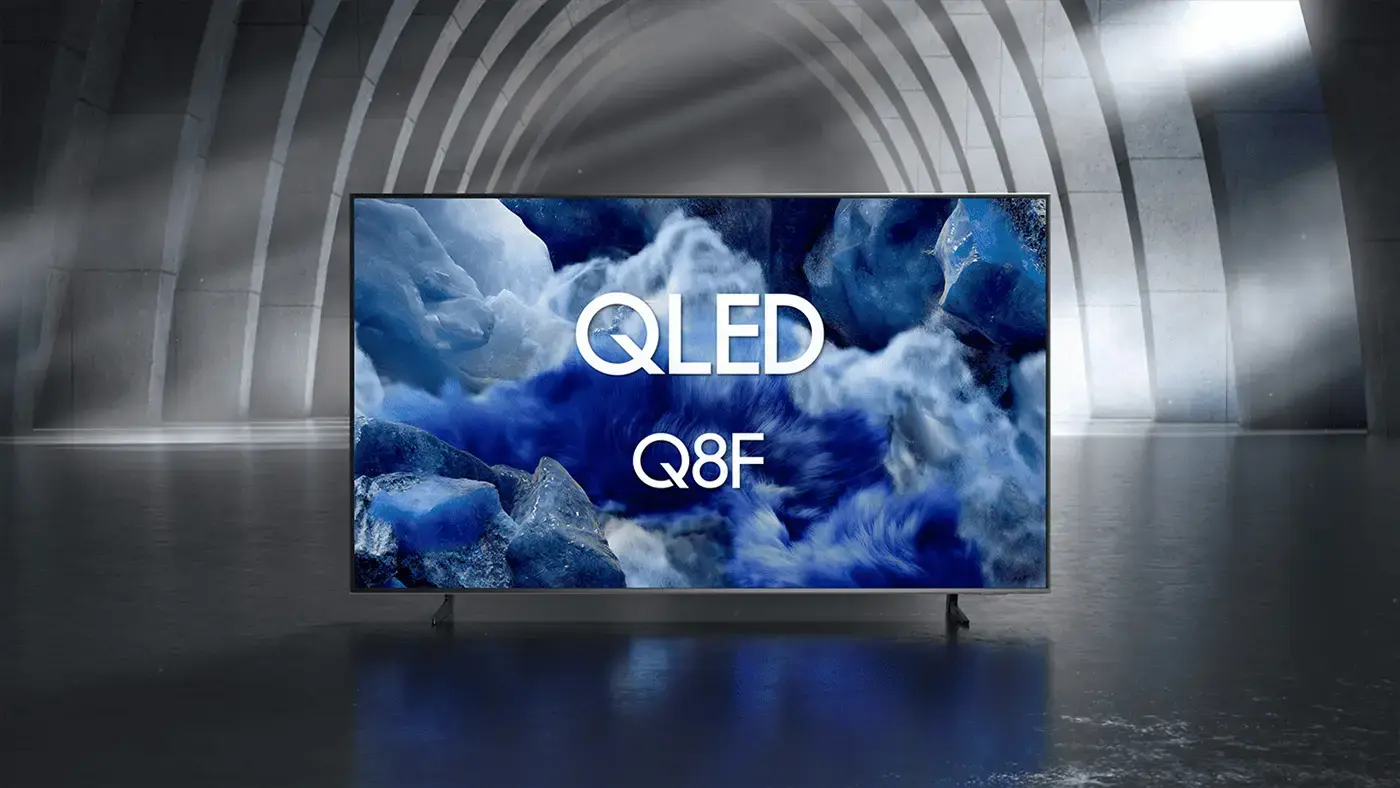 1400x788 qled q8f Telewizor z wyświetlaczem QLED pokazuje obraz z niebieskimi i białymi chmurami oraz tekstem \'QLED Q8F\'. W tle widoczne są łukowate struktury architektoniczne.