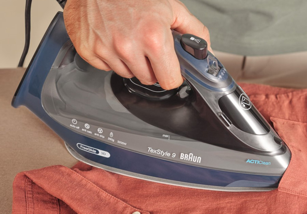 Osoba prasuje brązową koszulę żelazkiem BRAUN TexStyle 9. Na żelazku widoczne są napisy: \'TexStyle 9 BRAUN\', \'FreeGlide 3D\', \'ACTIClean\'.