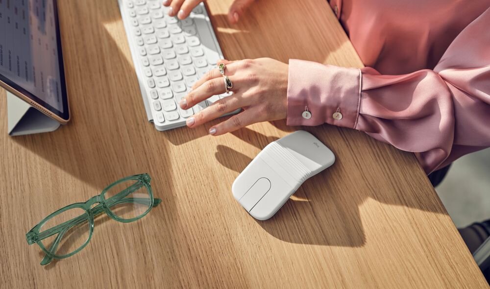 LOGITECH Mobi Fold - bezprzewodowa myszka leżąca na drewnianym biurku obok laptopa