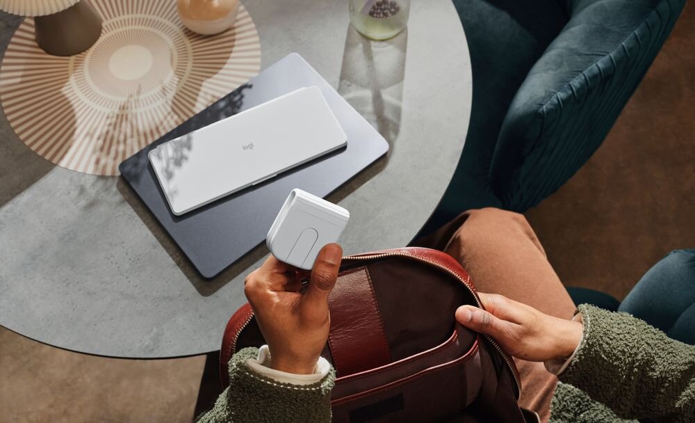 LOGITECH Mobi Fold Logitech Mobi Fold bezprzewodowa mysz Niewielka konstrukcja możliwość złożenia - Dłonie wkładające złożoną w kostkę myszkę bezprzewodową do skórzanego plecaka przy okrągłym stoliku
