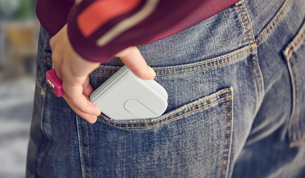 LOGITECH Mobi Fold Logitech Mobi Fold płaską konstrukcję 5,7 × 6,6 × 2,1 cm Silikonowy pokrowiec zawiasy - Zbliżenie na dłoń wsuwającą złożoną, niewielką myszkę bezprzewodową do tylnej kieszeni spodni z klasycznego denimu