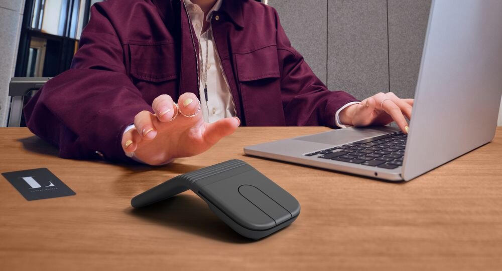 LOGITECH Mobi Fold touchpada Logitech Mobi Fold ograniczyć obciążenie mięśni przedramienia o 22% wbudowanego gładzika -Płaska mysz bezprzewodowa na drewnianym biurku obok dłoni piszących na klawiaturze oraz okularów korekcyjnych 