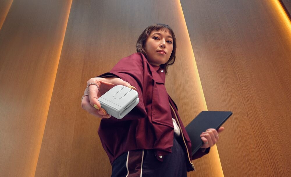 LOGITECH Mobi Fold Akumulator Logitech Mobi Fold przewodu USB-C Minuta ładowania 22 godzin pracy pełne naładowanie do miesiąca - Osoba trzymająca w wyciągniętej dłoni złożoną do formatu kostki mysz, z komputerem przenośnym pod ramieniem