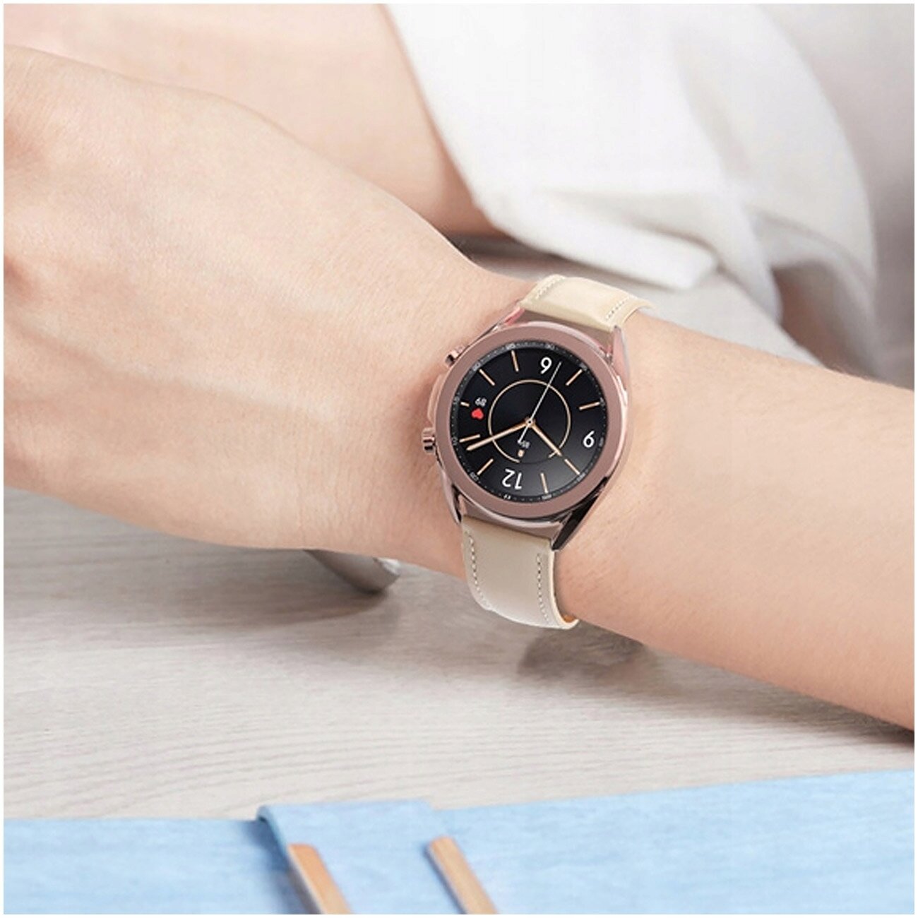 Na zdjęciu widoczny jest smartwatch z okrągłą tarczą i jasnym skórzanym paskiem na nadgarstku. Tarcza zegarka ma ciemne tło z jasnymi wskazówkami i cyframi.